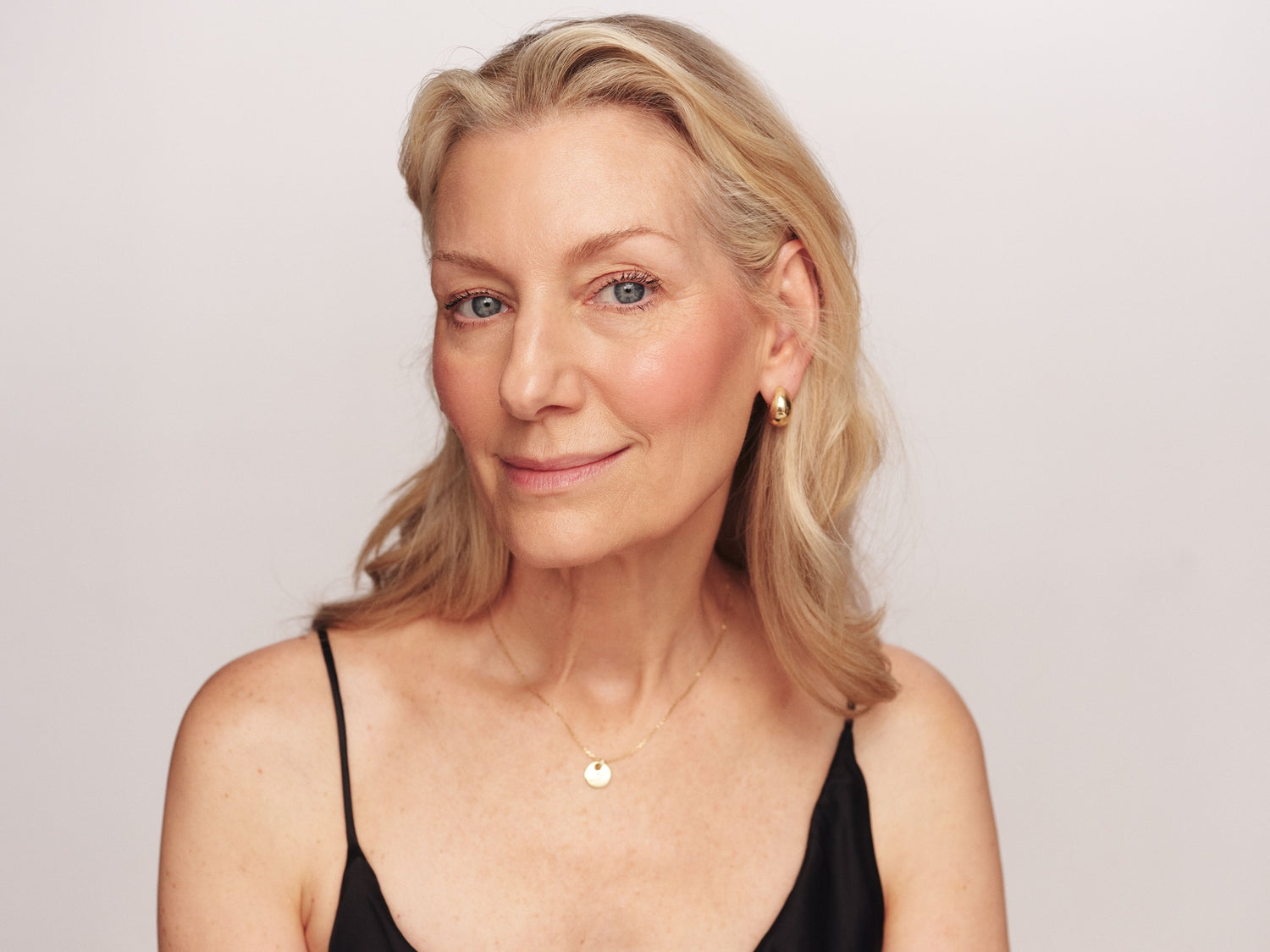 Woman with blonde hair and a black top against a plain background