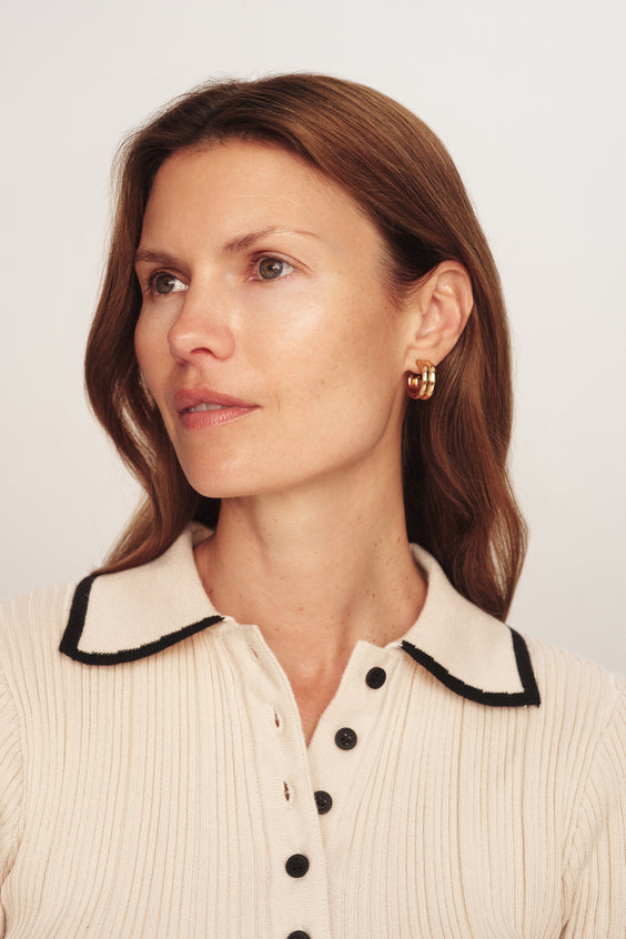 Woman wearing a cream-colored blouse with black trim and buttons on a plain background