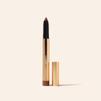 Mauve Eye Perfecting Shimmer Stick in a sleek gold tube with cap beside it on a minimalist cream background.