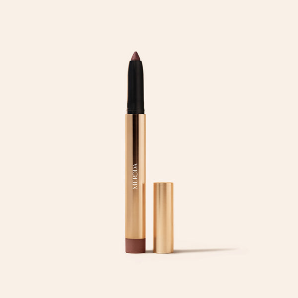 Mauve Eye Perfecting Shimmer Stick in a sleek gold tube with cap beside it on a minimalist cream background.