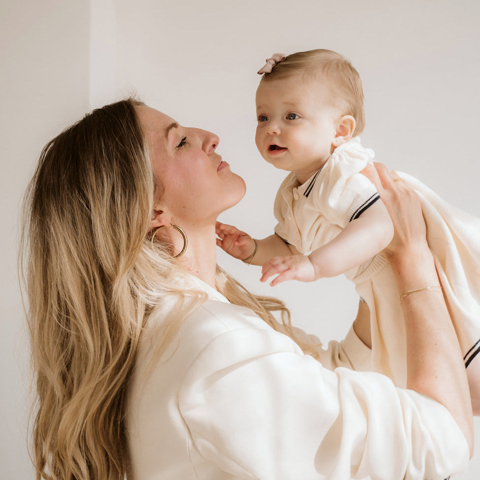 Woman holding a baby and looking at each other against a plain background