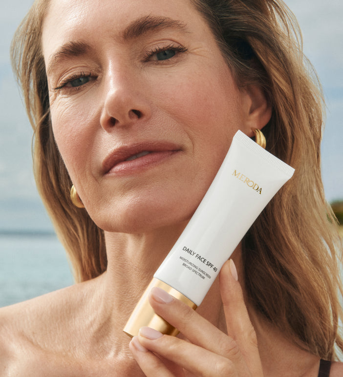 Daily Face SPF 40 sunscreen tube held by a model with radiant skin in a sunny, beach lifestyle setting.