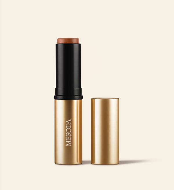 Soft Tan Bronzer stick in shade Dark shown upright with its gold cap placed neatly beside it.
