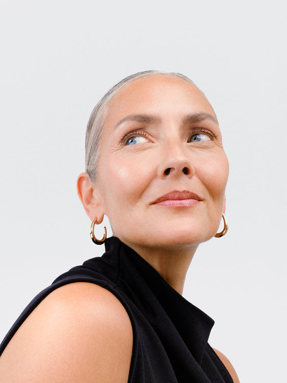 Woman with gray hair wearing a black sleeveless top against a light gray background